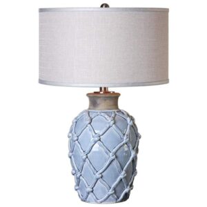 Pale blue ceramic table lamp on a white linen nightstand in a coastal bedroom