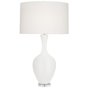 Terracotta table lamp with white linen shade beside cream bedding and rattan basket on a warm wood nightstand