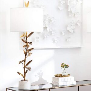 Wall sculpture art — aged brass column lamp beside an abstract metal wall panel in a contemporary living room
