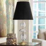 Metal table lamps on a side table — aged brass ceramic column lamp beside a sofa with books and a small plant