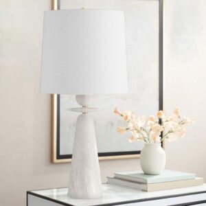 Sculptural floor lamp — aged brass column table lamp on a side table beside where a sculptural floor lamp would anchor the living room corner