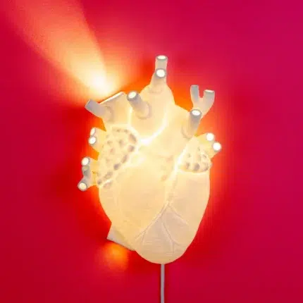 Heart wall lamp glowing warm white above a bed at night