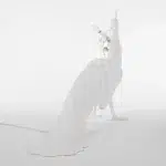 White peacock floor lamp glowing warm beside a bathtub at night