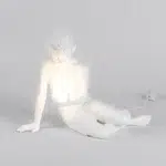 Sculptural table lamp of a white resin boy cradling a glowing orb