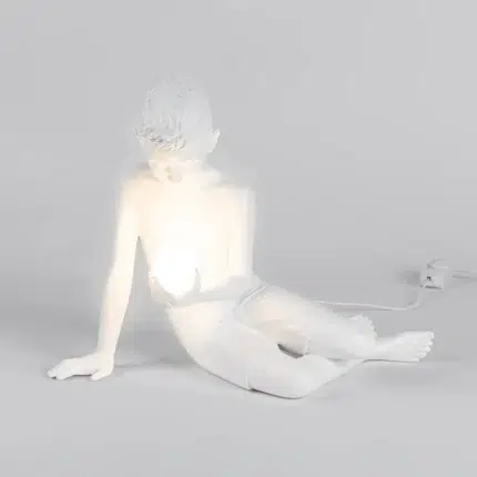 Sculptural table lamp of a white resin boy cradling a glowing orb