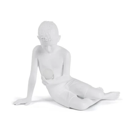 White boy-with-orb sculpture lamp glowing softly on a bedside table